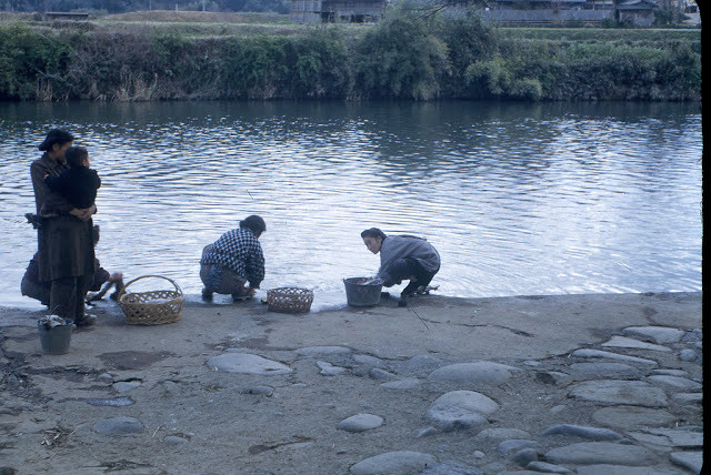 Những phụ nữ ngồi giặt giũ và trò chuyện bên bờ sông.