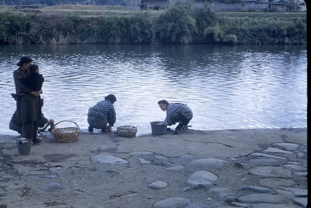 Những phụ nữ ngồi giặt giũ và trò chuyện bên bờ sông.