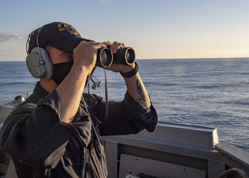 Một thủy thủ quan sát mặt biển bằng ống nhòm. Kể từ khi được đưa vào hoạt động từ năm 2003, USS Mustin chưa tham gia nhiệm vụ chiến đấu thực tế nào, nhưng đã thực hiện nhiều nhiệm vụ hỗ trợ nhân đạo ở Thái Lan và Myanmar.