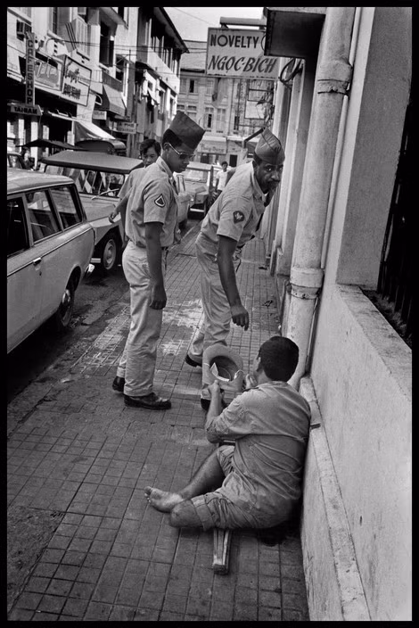 Một người ăn xin cụt chân mặc quân phục sĩ quan Sài Gòn xin tiền hai nhân viên quân sự Mỹ. Ảnh: Magnumphotos.com.