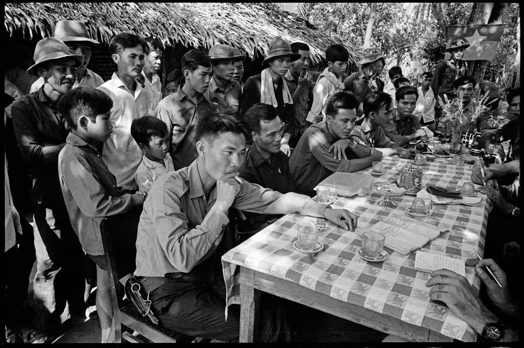 Người chỉ huy đội du kích trong buổi nói chuyện ngoài trời với các nhà báo nước ngoài. Ông đeo một khẩu súng sản xuất từ thời kháng chiến chống Pháp, xung quanh là đồng đội và dân làng. Ảnh: Magnumphotos.com.