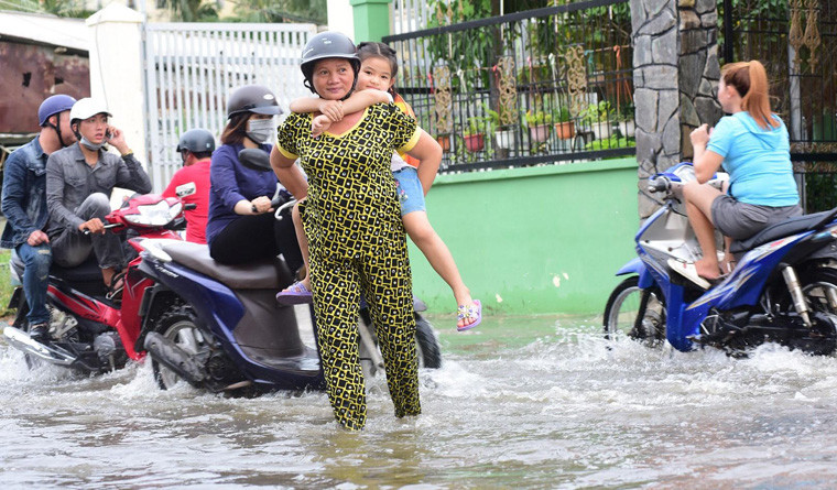 Trẻ tan trường được người lớn đưa qua vùng ngập nước ở huyện Nhà Bè, TP.HCM.