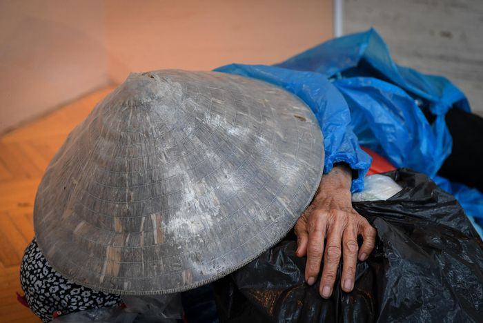 Một người vô gia cư mặc áo mưa rách, ngủ bên ngoài trung tâm thương mại ở đường Bà Triệu. Nhiệt độ về đêm ở Hà Nội có thể xuống đến mức 11-12 độ C.