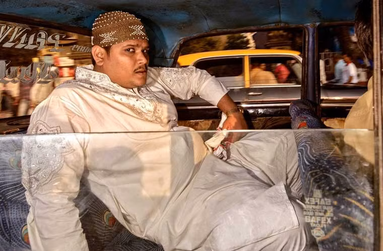 Nam hành khách ngồi thoải mái ở ghế sau taxi hướng mắt nhìn theo ống kính máy chụp.