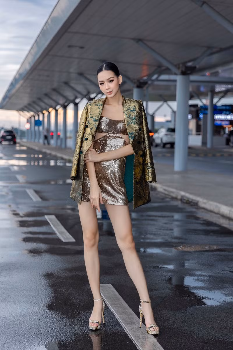 Xuất hiện tại sân bay, Á hậu Bảo Ngọc diện bộ đầm cocktail lấp lánh kèm theo chiếc áo khoác với họa tiết màu vàng đồng tạo điểm nhấn cho cả set đồ.