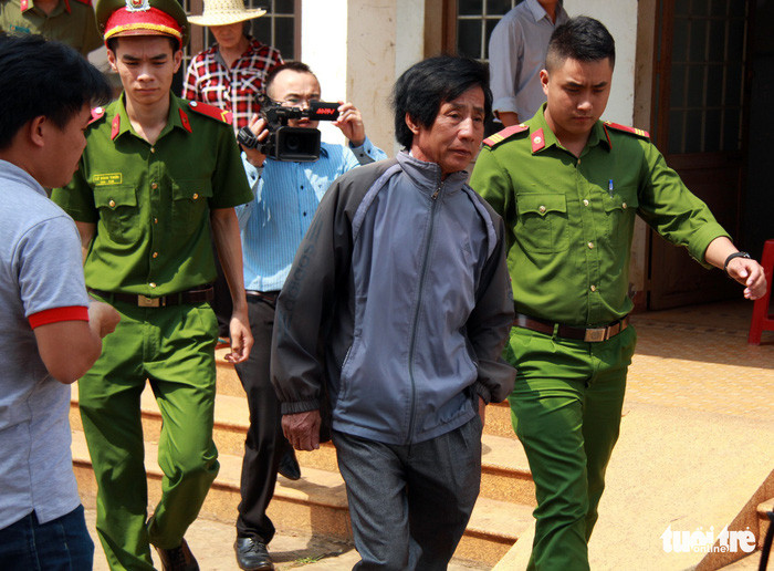 Ông Huỳnh Bê bị dẫn giải từ trụ sở UBND xã Hòa An về nhà để công an thực hiện lệnh khám xét - Ảnh: TRUNG TÂN