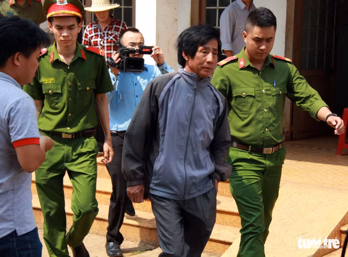 Ông Huỳnh Bê bị dẫn giải từ trụ sở UBND xã Hòa An về nhà để công an thực hiện lệnh khám xét - Ảnh: TRUNG TÂN