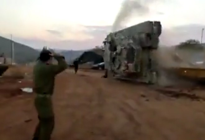 Hai người đứng ở đầu xe hướng dẫn tài xế vội vã tháo chạy, trong khi chiếc xe tăng chồm lên, lao vào gờ cản phía trước, đổ nghiêng sang bên trái và lật ngửa.