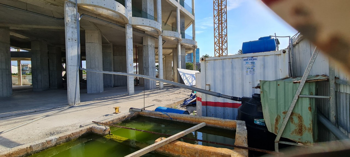 Phía sau hàng rào tôn kín mít là ngổn ngang các dụng cụ, vật liệu xây dựng, cạnh hồ nước mưa ngay chân công trình.