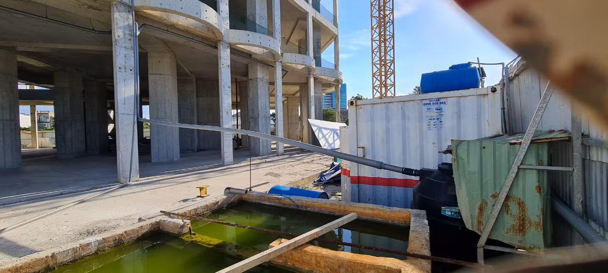 Phía sau hàng rào tôn kín mít là ngổn ngang các dụng cụ, vật liệu xây dựng, cạnh hồ nước mưa ngay chân công trình.