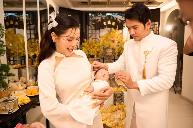 Lý Bình đeo dây chuyền vàng cho bé Loka. Nam diễn viên viết: "Mừng con trai Loka Quan của ba đầy tháng. Chúc con bú giỏi, ngủ giỏi, khỏe mạnh, mau ăn chóng lớn để chơi với anh ba Tyga Quan và chị 2 Mia Soma".