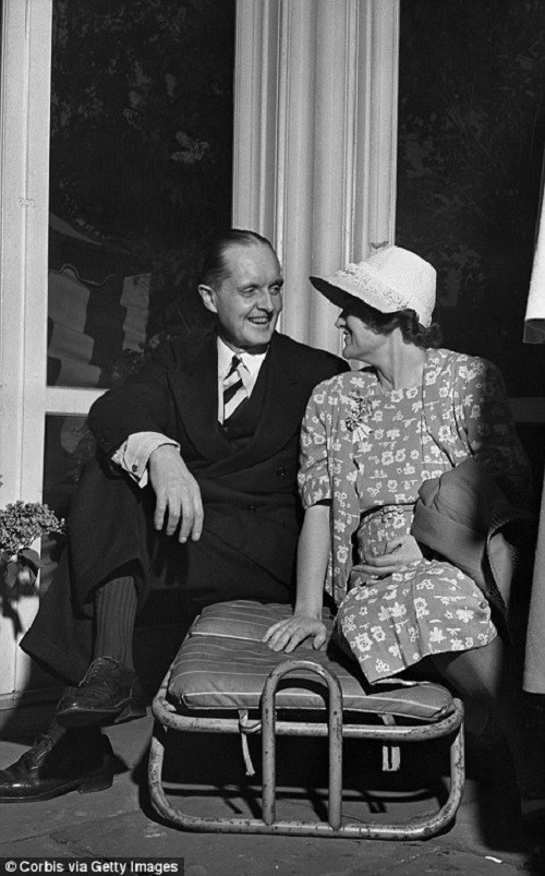 Một cặp đôi ngồi trên chiếc ghế dài bên ngoài một khách sạn.