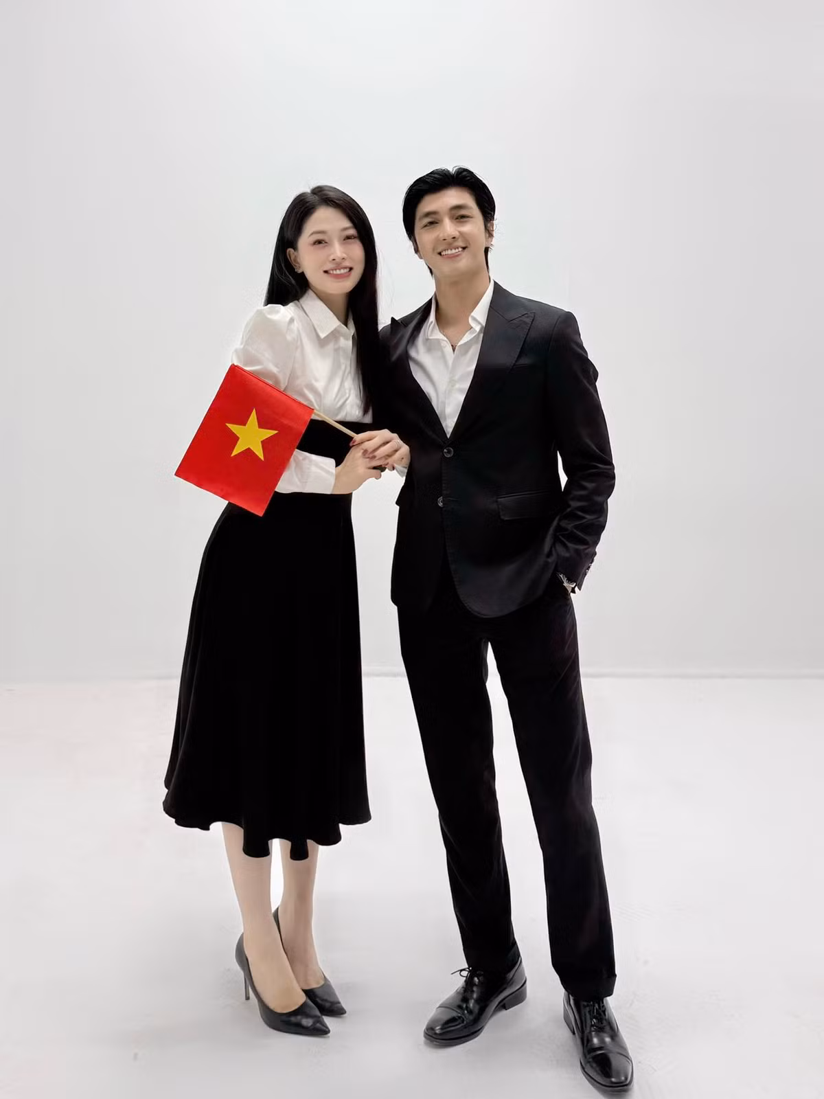 Vợ chồng Bình An - Phương Nga diện trang phục tone đen trắng, chụp ảnh với lá cờ đỏ sao vàng. Ảnh: FB Nguyễn Bình An