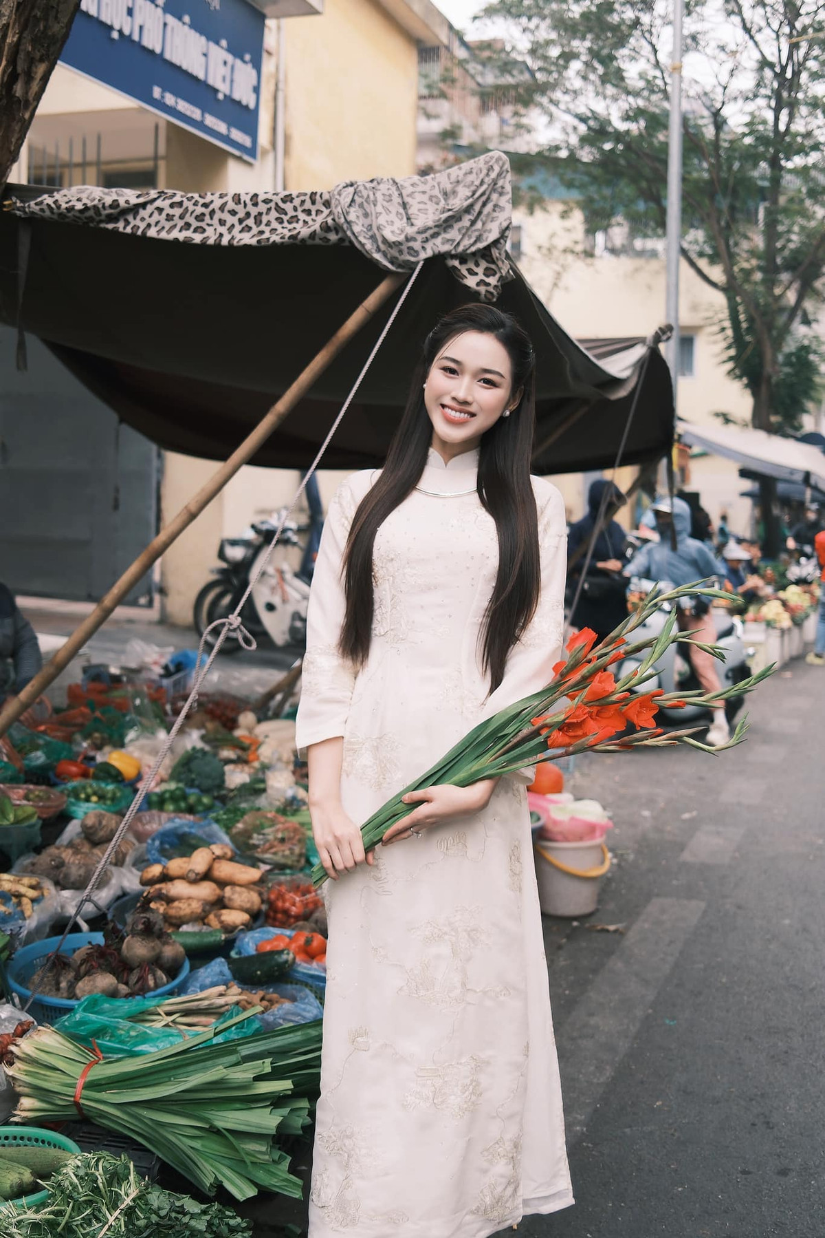 Hoa hậu Đỗ Thị Hà trong tà áo dài trắng thướt tha, nổi bật với vẻ đẹp dịu dàng, nền nã giữa không gian chợ Tết mộc mạc, gần gũi. Ảnh: FB Đỗ Thị Hà