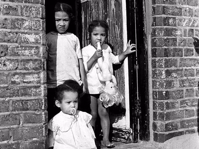 Ba em nhỏ đứng trước cửa nhà. Ảnh: Vintage.