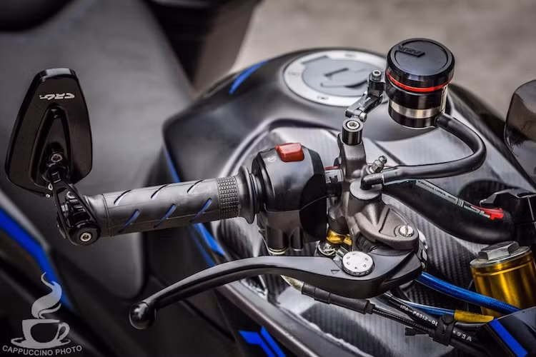 Toàn bộ dàn đầu xe cũng được nâng cấp full với chảng 3 kèm cặp phuộc USD của Honda CB190R, sau đó hạ phuộc thêm khoảng hơn 3 cm để xe "đầm" hơn. Nằm phía trên tay lái của xe là cặp bao tay Domino cùng gương gắn gù CRG.