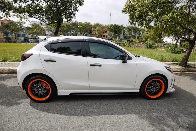 Ở hai bên hông, chiếc Mazda 2 đã có thêm cặp gương với 4 chức năng trong 1 và có lớp vỏ ngoài bằng sợi carbon. Dọc theo thân xe là nẹp hông thể thao, trong khi bộ mâm nguyên bản của xe đã được thay bằng mâm nhiều nan thể thao với vành sơn màu cam nổi bật.