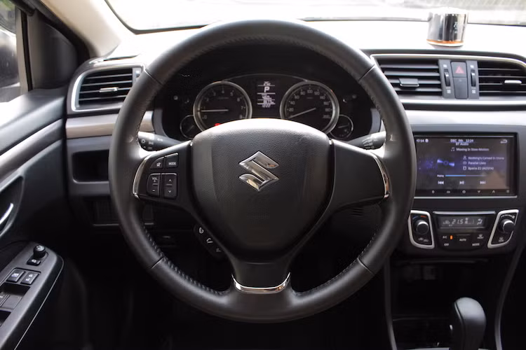 Dù nằm trong phân khúc xe giá rẻ nhưng Ciaz vẫn có vô-lăng 3 chấu "gật gù" và tích hợp các cụm nút thoại, chỉnh âm thanh ở chấu bên trái. Một điểm trừ nhỏ của xe đó là cụm nút điều khiển thoại trên vô-lăng gồm 3 nút kết nối bluetooth - nhấc máy - dập máy bị đặt quá sâu ở bên dưới, khó với ngón cái xuống khi đang cầm lái. Ngoài ra, cụm nút điều khiển âm thanh không có nút Play/Pause.