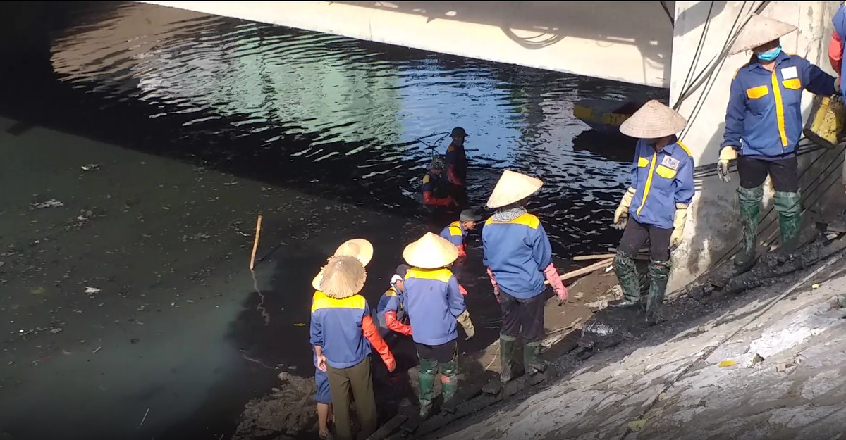 Các công nhân xếp thành hàng dài từ dưới lòng sông lên đến vỉa hè để chuyền tay nhau những xô bùn, đất được múc từ dưới sông đưa lên.