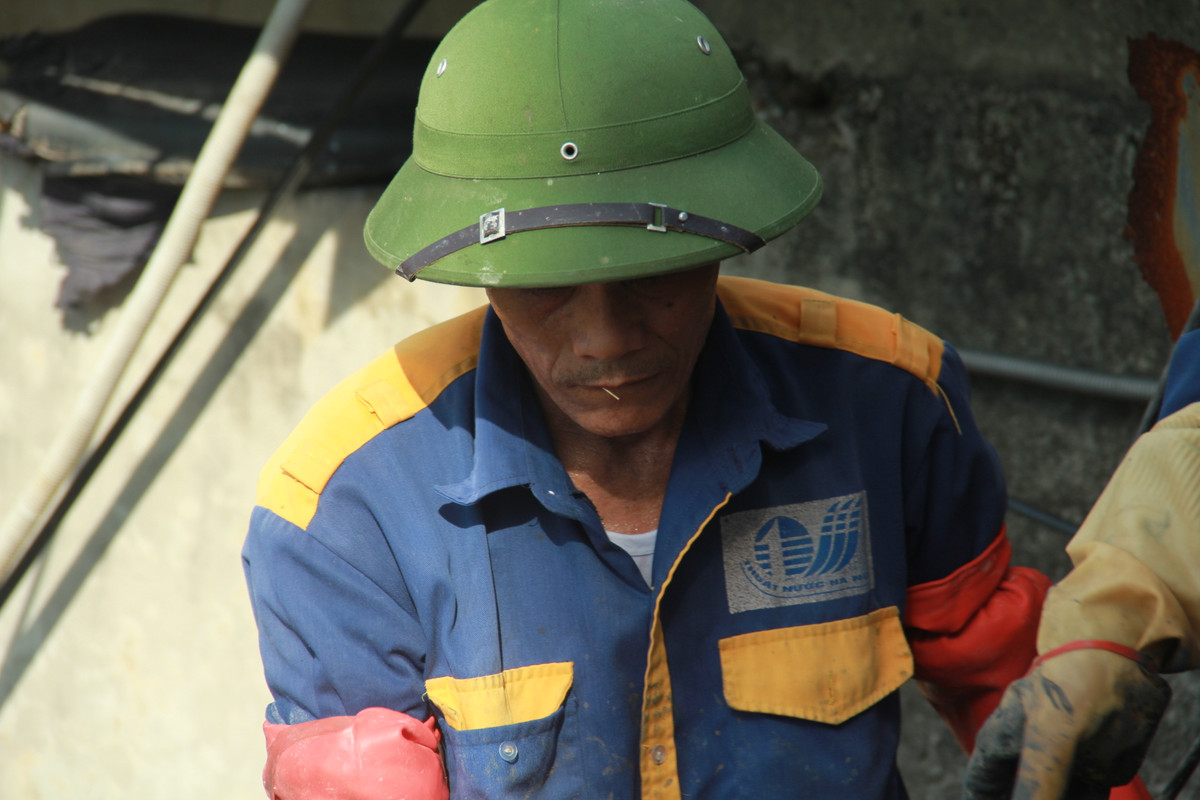 Nét mệt nhọc thấm trên mặt người đàn ông dưới chiếc mũ cối che nắng.