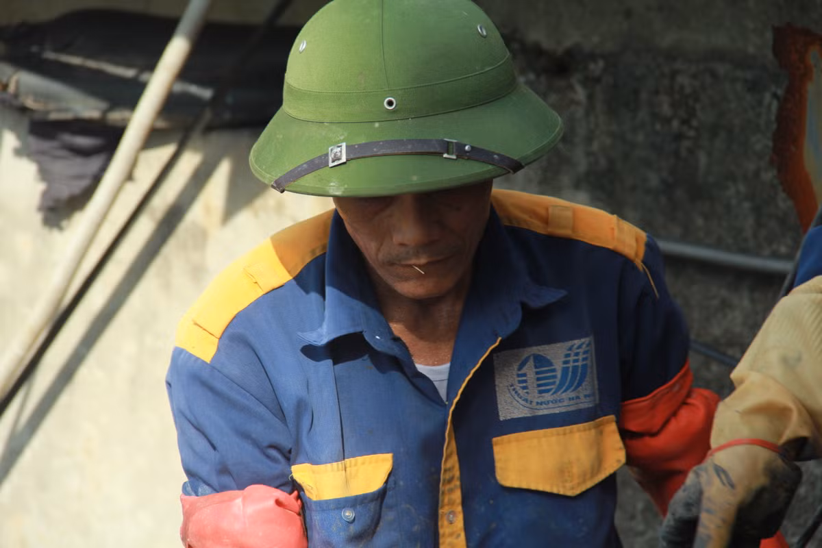 Nét mệt nhọc thấm trên mặt người đàn ông dưới chiếc mũ cối che nắng.