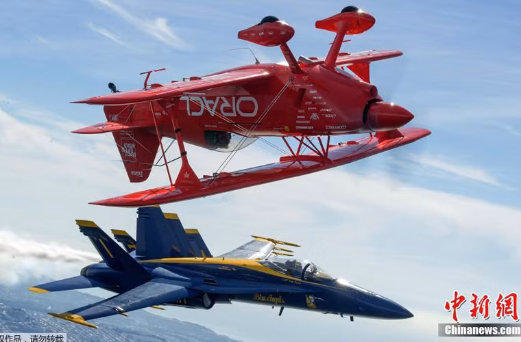 Tiêm kích hạm F/A-18 của đội bay “Thiên thần xanh” (Blue Angels) đang nhào lộn cùng một chiếc máy bay hai tầng cánh.