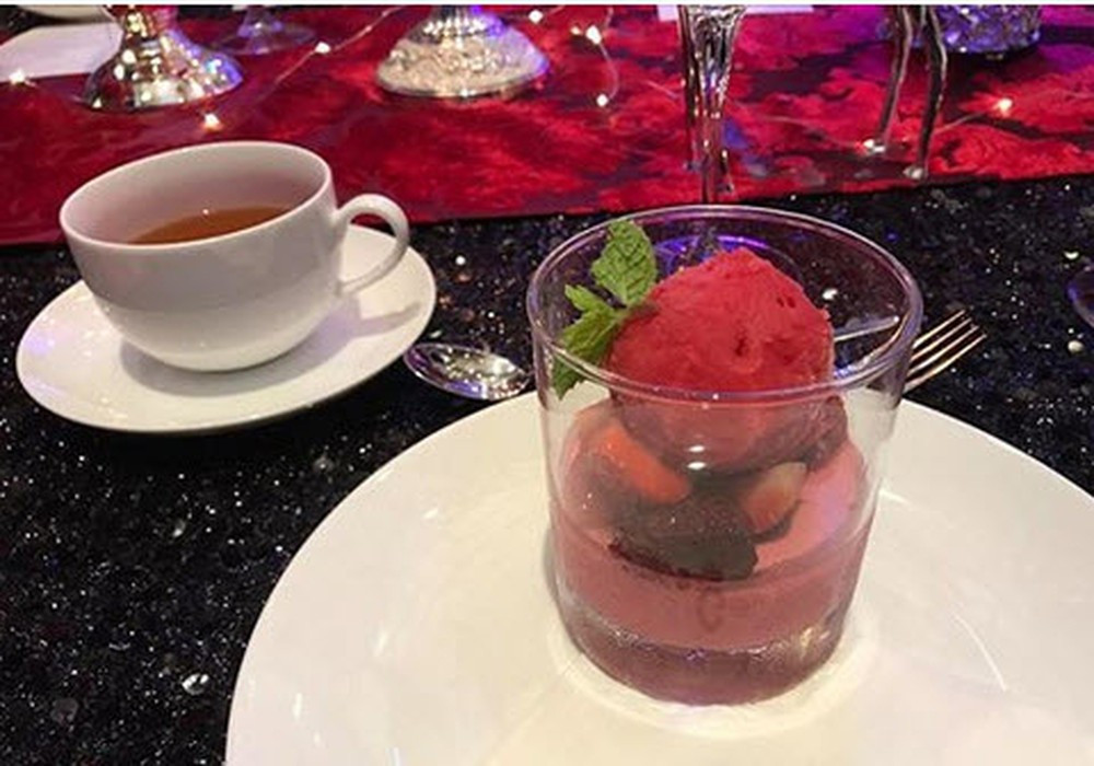 Món tráng miệng: Panna cotta kem blackcurrant (quả lý chua đen) và trà nóng. Lý chua đen (hay blackcurrant) là một loại cây bụi bản địa của một số vùng Trung Âu, Bắc Âu và Bắc Á. Cây ưa lạnh, ra nhiều quả thành chùm dọc thân vào mùa hè. Quả lý chua đen giàu vitamin C, chất dinh dưỡng và chất chống oxy hóa. Trong tiệc cưới, đây là nguyên liệu làm thành món kem, phía dưới là panna cotta kiểu Italy.