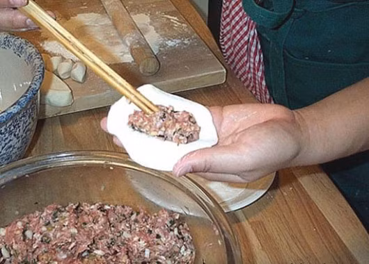 Gói bánh: Đặt miếng bột trên mặt phẳng và cho nhân thịt vào giữa, thêm 1 quả trứng cút rồi xếp vỏ bánh lại, kẹp mép theo hình vắt chéo sao cho mép bột dính lại với nhau và đẹp mắt là được. 