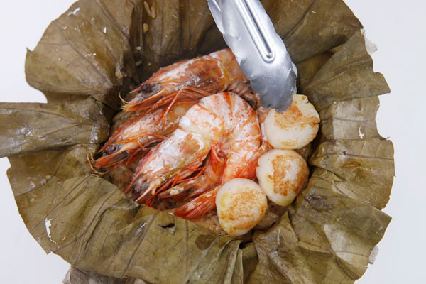 Trong thời gian chờ xôi chín, chao tôm và sò điệp trên chảo nóng. Nếu không thích chao tôm, bạn có thể xếp tôm và sò lên trên cùng của gạo và hấp cùng xôi, nước tôm hấp chảy xuống cũng sẽ giúp xôi có vị ngọt hơn. Nhấc cả bọc lá sen ra đĩa, xếp tôm, sò lên trên, rắc thêm hành lá, cần tây để trang trí.