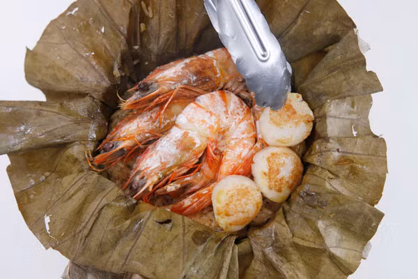 Trong thời gian chờ xôi chín, chao tôm và sò điệp trên chảo nóng. Nếu không thích chao tôm, bạn có thể xếp tôm và sò lên trên cùng của gạo và hấp cùng xôi, nước tôm hấp chảy xuống cũng sẽ giúp xôi có vị ngọt hơn. Nhấc cả bọc lá sen ra đĩa, xếp tôm, sò lên trên, rắc thêm hành lá, cần tây để trang trí.