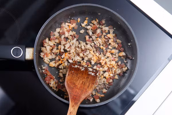 Làm nóng chảo ở nhiệt độ cao, phi tỏi thơm sau đó cho tôm, nấm và lạp xưởng vào xào. Cho gạo nếp và 100ml nước dùng gà vào chảo, đảo qua để tôm, nấm, lạp xưởng lẫn đều vào gạo, đậy nắp nấu khoảng 5 phút để gạo hấp thụ hết nước dùng.