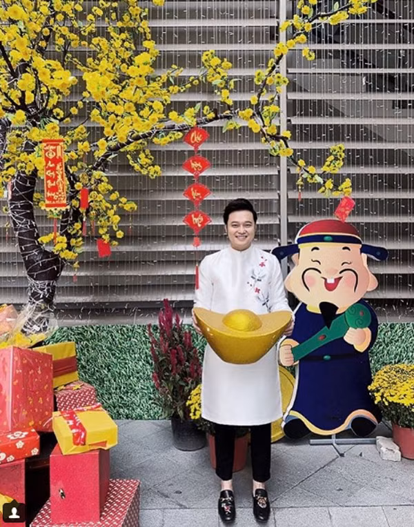 Ca sĩ Quang Vinh vẫn vô cùng trẻ trung với áo dài màu trắng thêu hoa đơn giản, phối cùng quần âu đen và giày hiệu.