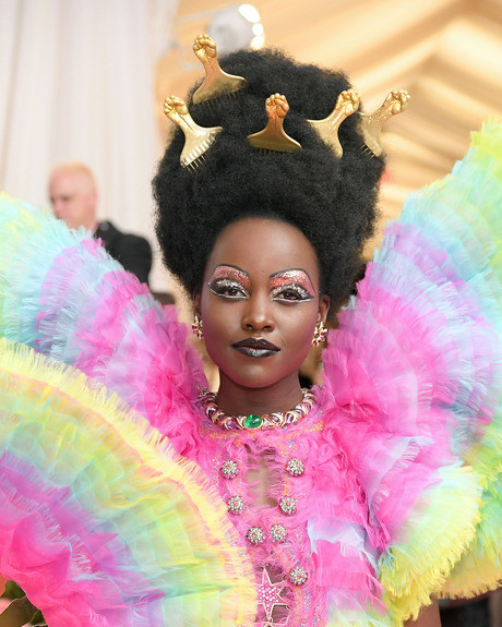 Lupita Nyong'o thu hút sự chú ý ở thảm đỏ Met Gala với khuôn mặt trang điểm ánh nhũ, tóc đánh bông xù, tô điểm bằng những chiếc lược hình nắm tay. 