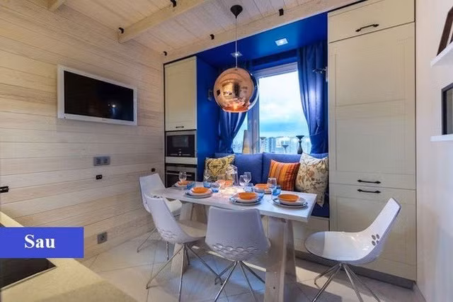 Sau khi được cải tạo, không gian bếp đã trở nên rộng rãi và thông thoáng hơn. Toàn bộ gian phòng được chủ nhân ốp gỗ thông với tông trắng chủ đạo. Trên nền đó, sử dụng khung cửa, rèm và nệm ghế màu xanh biển đậm tạo điểm nhấn. Bàn ăn được thay thế bằng thiết kế hiện đại hơn.