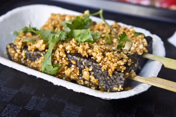 Trư huyết cao thường được cắt thành từng miếng hình chữ nhật hoặc hình tam giác, xiên một que tre vào chính giữa để thực khách có thể thoải mái vừa cầm trư huyết cao thưởng thức vừa dạo chợ hệt như đang ăn kem. Món này sẽ ngon hơn nếu bạn ăn cay. Ảnh: Internet.