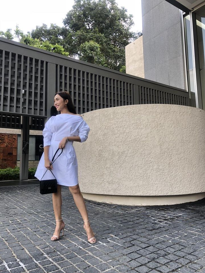 Váy trắng trễ vai phối với túi xách đen sành điệu.