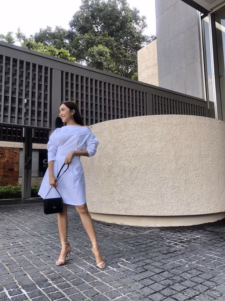 Váy trắng trễ vai phối với túi xách đen sành điệu.