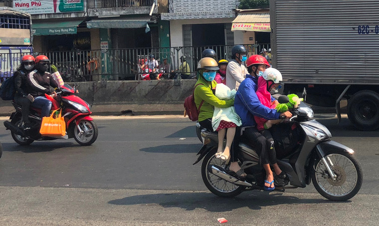 Nhiều đứa trẻ được cha mẹ trùm kín để che nắng, bụi trên chuyến đi bằng xe máy đưa cả nhà vể quê miền Tây đón Tết cổ truyền.