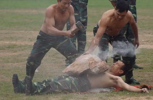 Nằm trên thủy tinh để cho xe máy cán qua người và làm “giá đỡ” đập vỡ tảng đá. Ảnh: TienPhong.