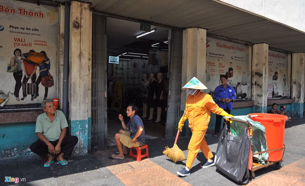 Ông Phục (bìa trái) và ông Hiệp ngồi nói chuyện với nhau tại một cửa ra vào chợ Bến Thành. 2 ông làm nghề chở hàng thuê bằng xe máy tại chợ. Nếu lúc trước các ông luôn bận bịu thì nay hoàn toàn trái ngược. Cả ngày 27/2, ông Phục và ông Hiệp chỉ chở được 2 cuốc xe hàng, thu nhập mấy chục nghìn đồng.