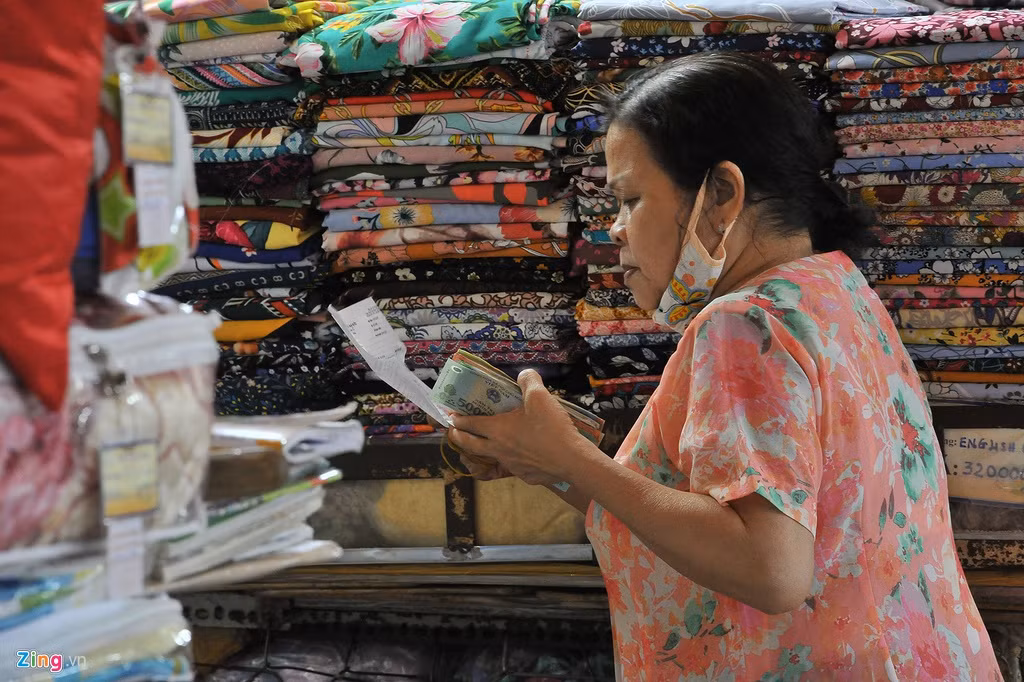 Bà Đậm xem hóa đơn tiền thuê sạp trong tháng. Sạp vải của bà lâm cảnh ế ẩm nhiều ngày. Bà cho biết gần 1 tháng qua, mỗi ngày bà chỉ bán được cho một vài khách, thu nhập chưa đến 200 nghìn đồng. "Dù sạp vải của tôi không lo lỗ vốn nhất thời, nhưng thu nhập như vầy rất khó để duy trì công việc. Đã nhiều năm làm nghề tại đây, tôi chưa rơi vào hoàn cảnh này", bà nói.