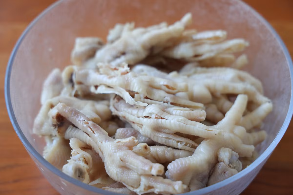 Bỏ chân gà đã róc xương vào âu. Chuẩn bị chanh, tỏi, ớt, rau mùi và mắm muối, nước tương tạo màu.