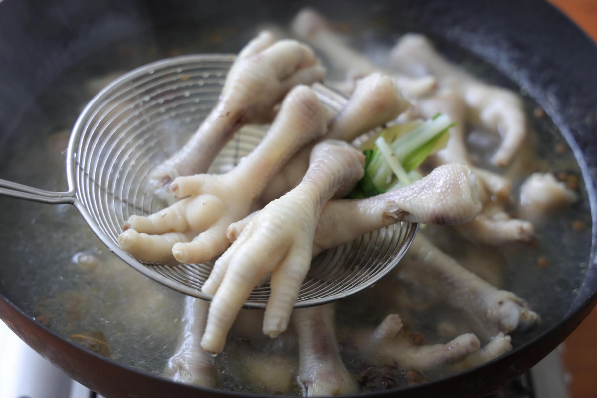 Sau khi cắt móng chân gà, đun sôi nước trong nồi, cho gừng, hành lá, ót, hoa hồi vào, sau đó cho chân gà vào nồi, đun khoảng 8 phút;