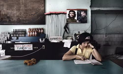 Nhân viên bán hàng kiểm tra sổ sách. Phía sau là ảnh chân dung người hùng Che Guevara được treo một cách trang trọng ở trên tường.