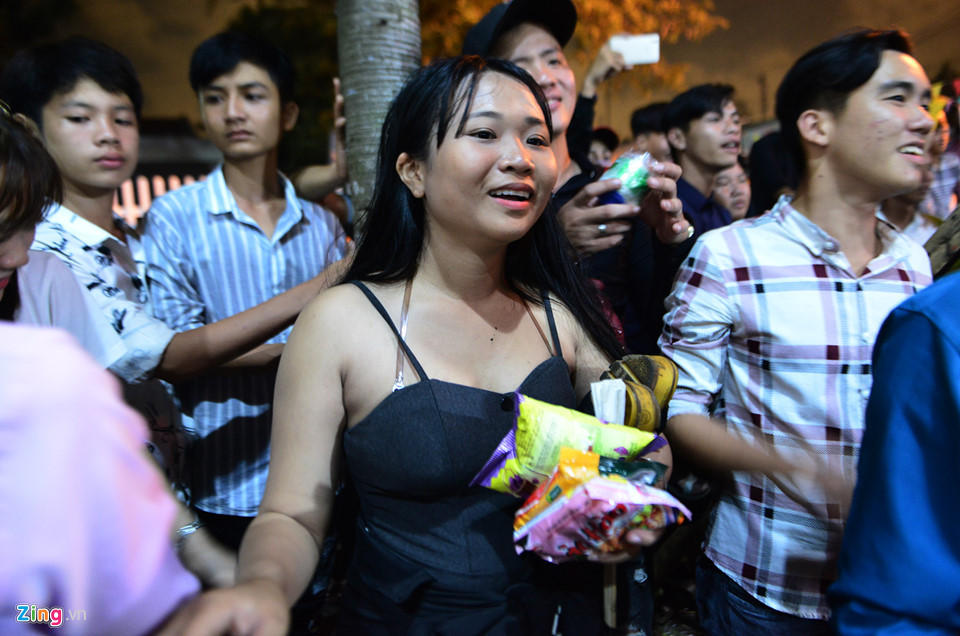 Cô gái ngụ huyện Châu Thành, Long An này phải kẹp dép bên nách cùng một số bánh trái thu được, đứng nhìn những người khác tranh giành bên trong.