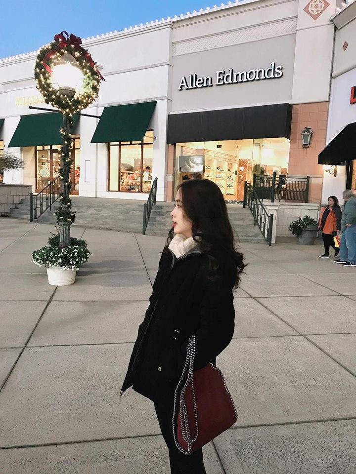 Cô mặc áo khoác đen, khăn trắng và túi xách màu đỏ đô rất phong cách.