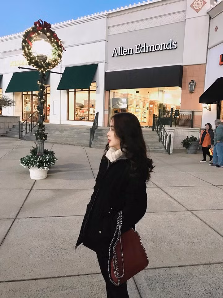 Cô mặc áo khoác đen, khăn trắng và túi xách màu đỏ đô rất phong cách.