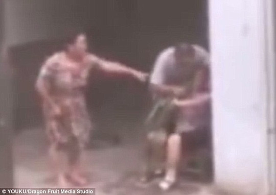 Ảnh cắt từ video cho thấy người con trai nhét cỏ vào miệng mẹ trong khi vợ anh ta đứng chỉ trỏ.