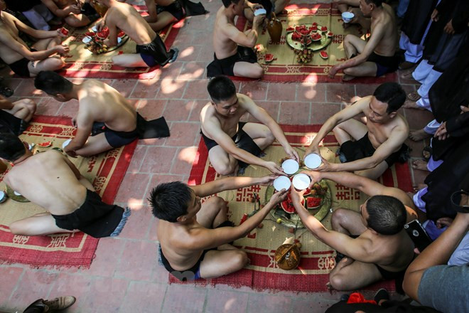Trước khi tham gia vật cầu các giáp làm lễ bái vào đình sau đó ngồi giữa sân đình, lúc này mỗi giáp uống một bình rượu lấy khí thế và ăn một quả dưa hấu để nhận được may mắn khi tham gia vật cầu. (Ảnh: Minh Sơn/Vietnam+)