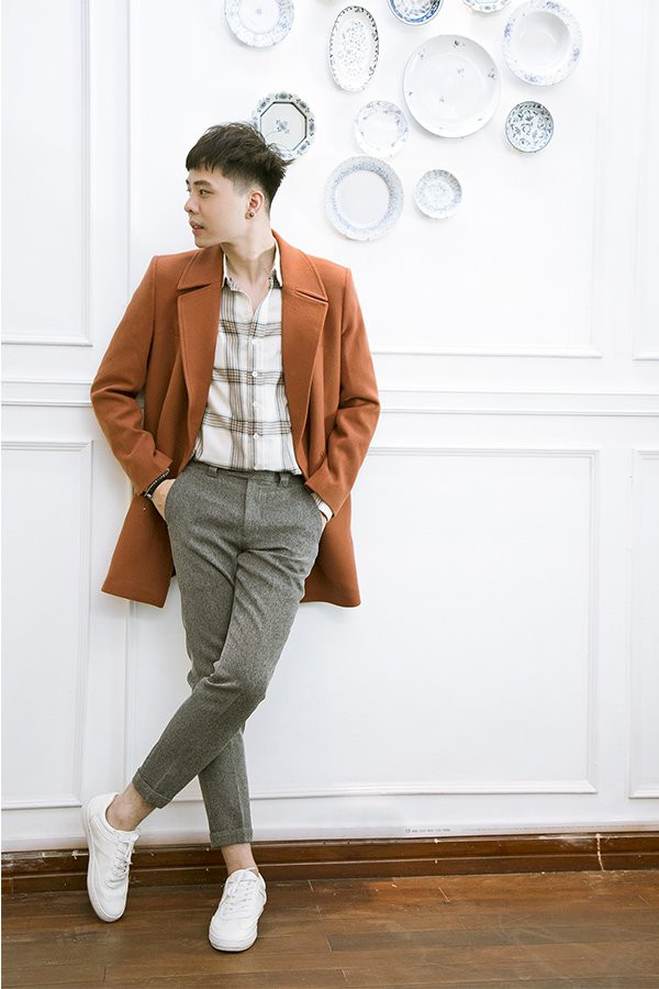 Nam ca sĩ phối áo sơ mi kẻ với quần vải xám và áo khoác dáng dài rất lịch lãm, trẻ trung.